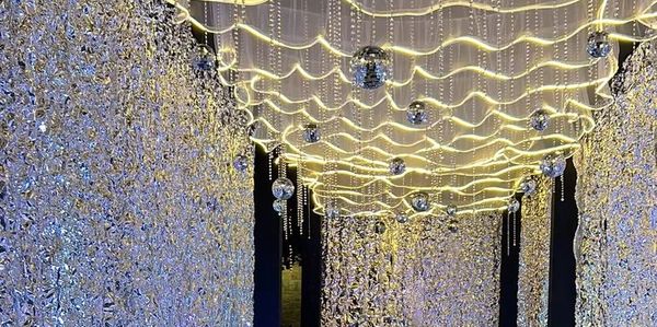 Elegant event walkway with shimmering walls, floral arrangements, and wavy ceiling lights.