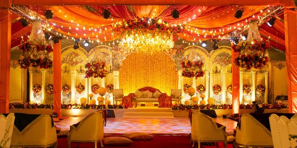 Lavishly decorated wedding stage with vibrant orange drapes and floral chandeliers.