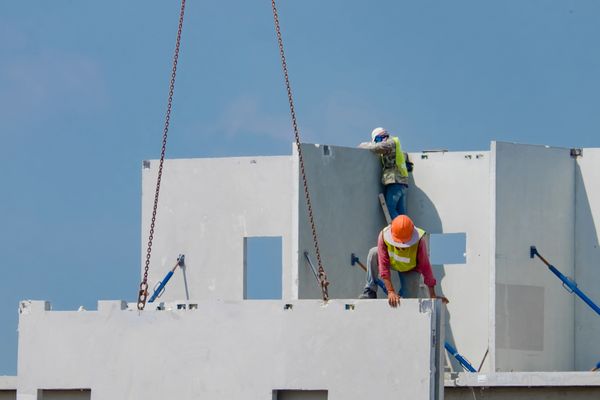 Construction workers installing large precast concrete panels on a building.