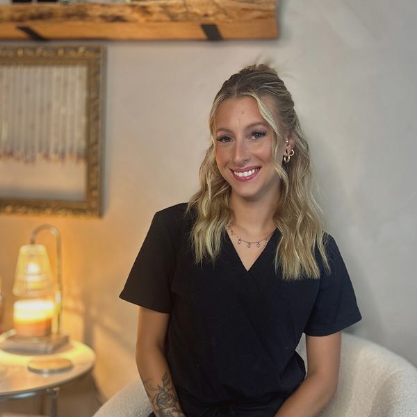 Smiling woman with wavy blonde hair and tattoos, sitting indoors.