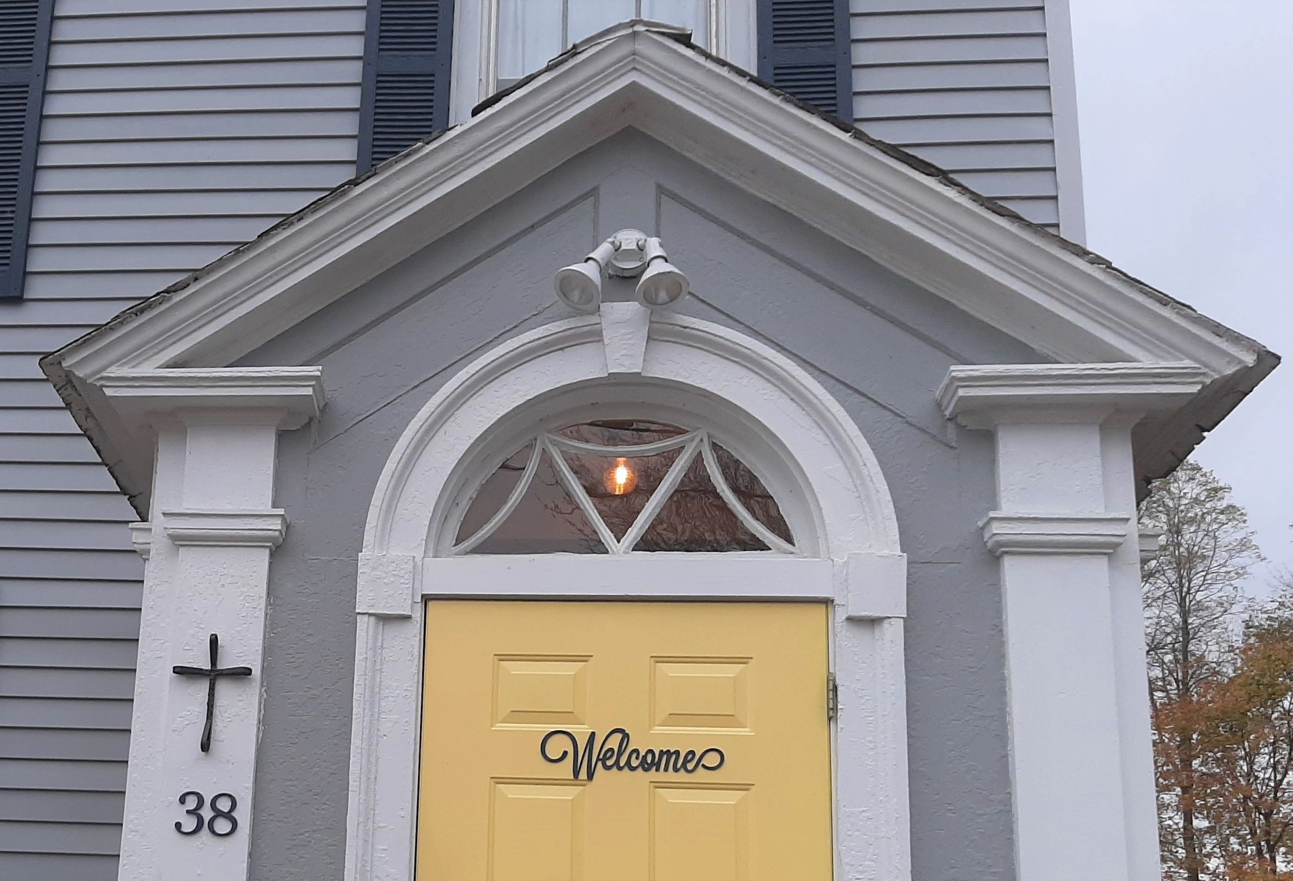 Yellow front door with welcome sign and decorative white trim.