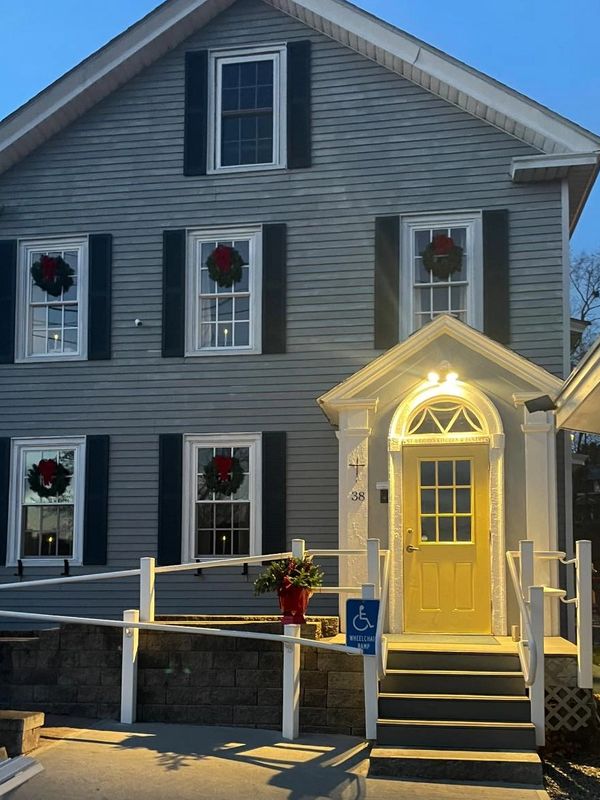 A gray house with holiday wreaths on windows and a well-lit yellow door with a ramp.