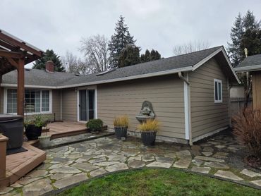 Backyard patio area with stone flooring and a beige house exterior on a cloudy day.