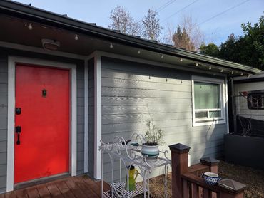 House exterior with a bright red door and a small white metal plant stand.