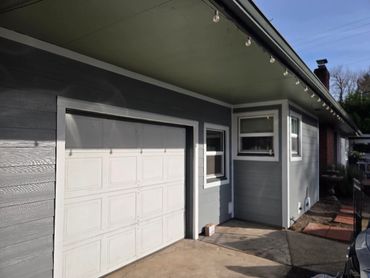 Gray house exterior with white garage door and string lights.