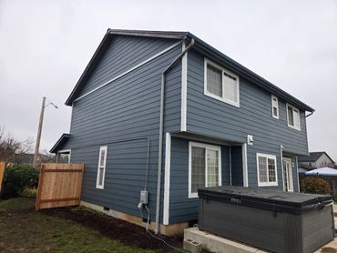 Two-story blue house with white trim and a covered hot tub outside.