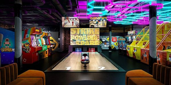 A neon-lit bowling alley with arcade games and seating areas.