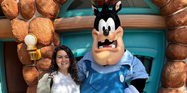Person posing with cartoon character Pete at a colorful stone and blue door backdrop.