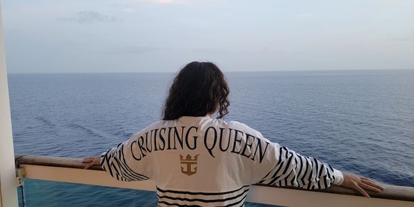 Person with striped shirt labeled 'CRUISING QUEEN' overlooking calm ocean from ship.