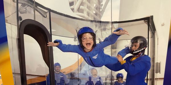 Child experiencing indoor skydiving with instructor support.