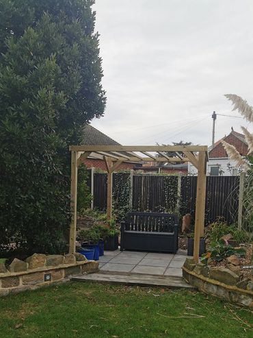 A wooden pergola with a black bench in a garden.