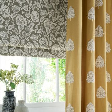 Window showing a  roman blind in a traditional floral design with a mustard yellow curtain in front.