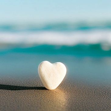 A heart-shaped stone on the sandy beach near the ocean.