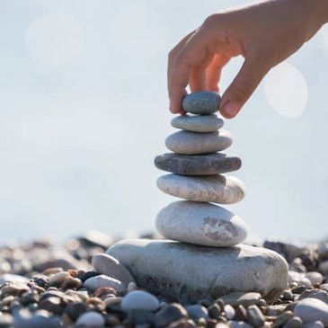 Hand stacking smooth stones on a pebble beach under soft light.