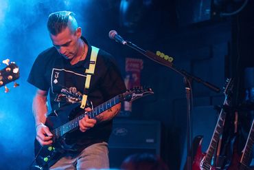 Guitarist intensely playing on stage with blue lighting and smoke effects.