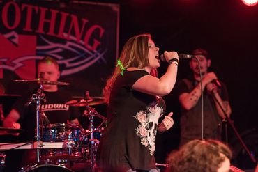 A woman passionately singing on stage with a band.
