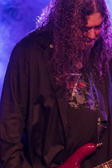 Musicians playing guitars on a smoky, purple-lit stage during a live performance.