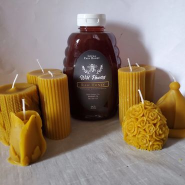 A bottle of raw honey surrounded by various yellow beeswax candles.