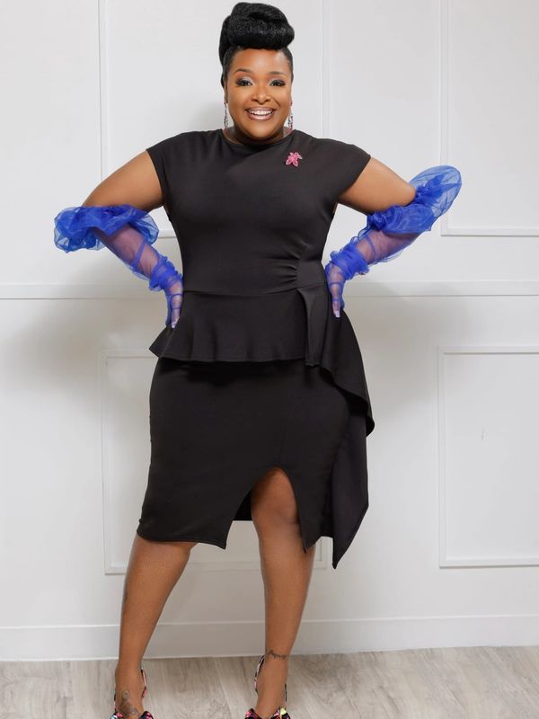 Woman in a black dress with blue gloves smiling.