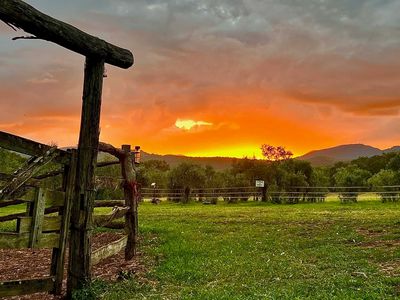 Sunset over a rustic wooden fence in a green field with hills in the background.