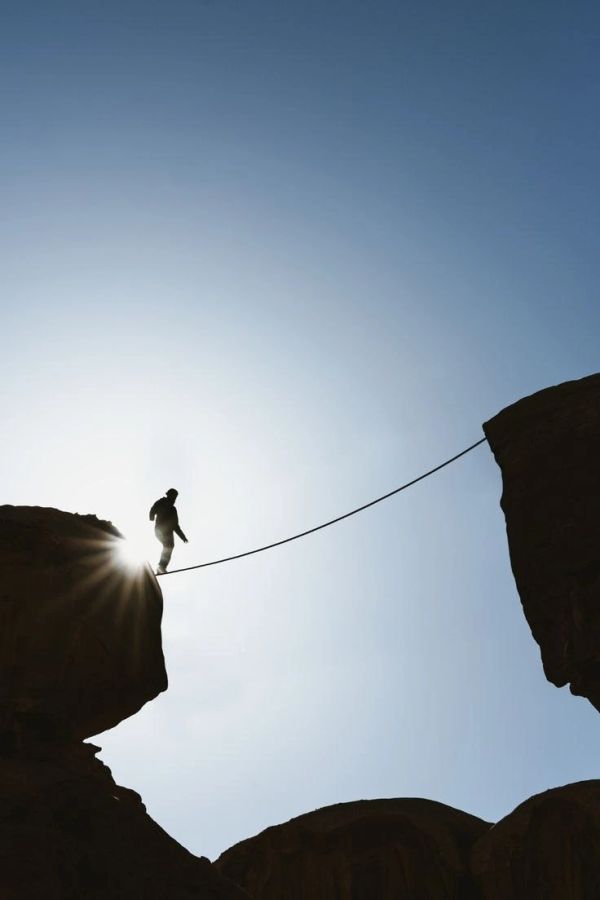 Person crossing a rope bridge between cliffs.