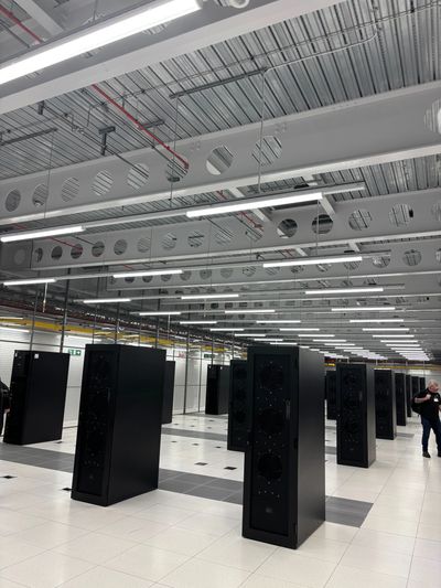 A modern data center with rows of black server racks and bright overhead lights.