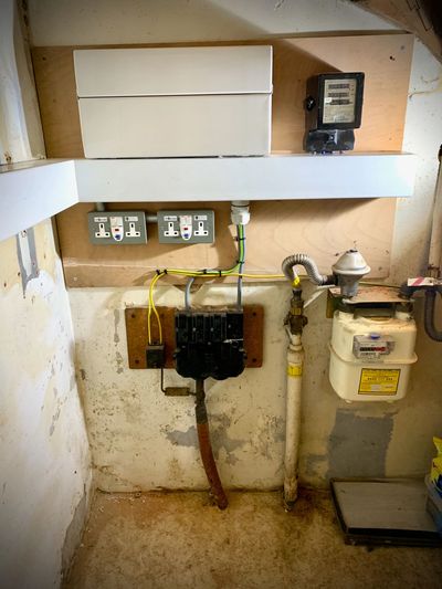Utility area with gas meter, electrical outlets, and wiring on a worn wall.