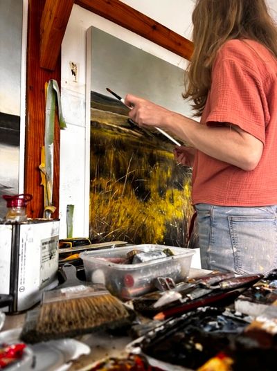 Artist painting a landscape in a studio.