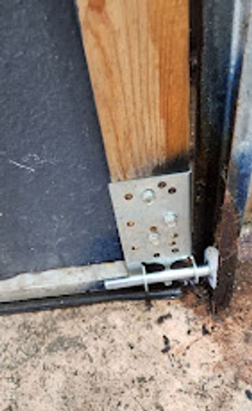 Close-up of a metal bracket securing a wooden post to a concrete floor.