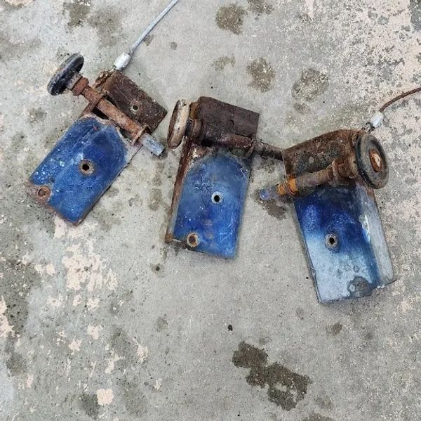 Three rusty blue metal brackets with attached round knobs on a concrete floor.