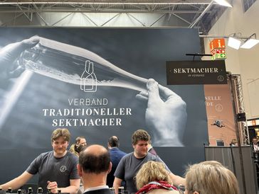 People at a booth with a large banner about traditional sparkling wine makers.