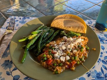 Pollo con Arroz, plated with sauteed green beans and corn tortillas.