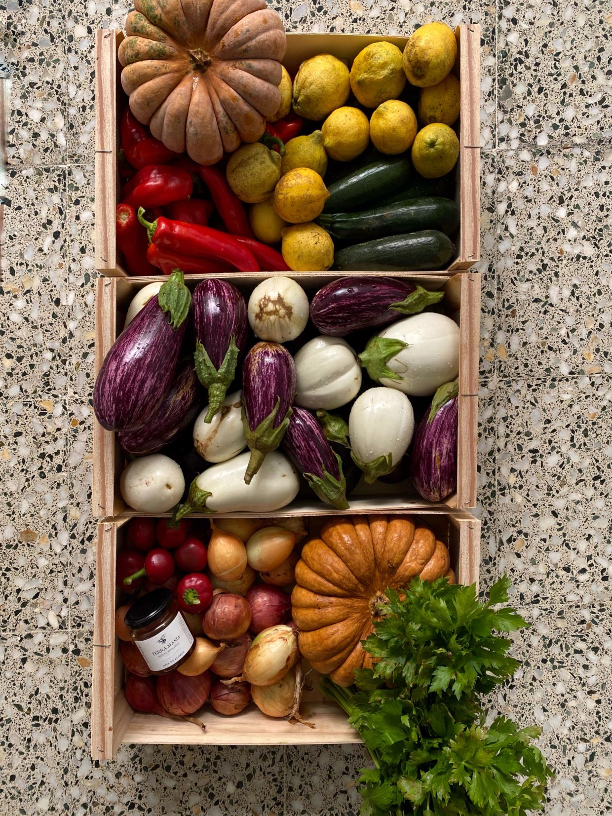 Wooden crates filled with assorted fresh vegetables and herbs on a stone floor.