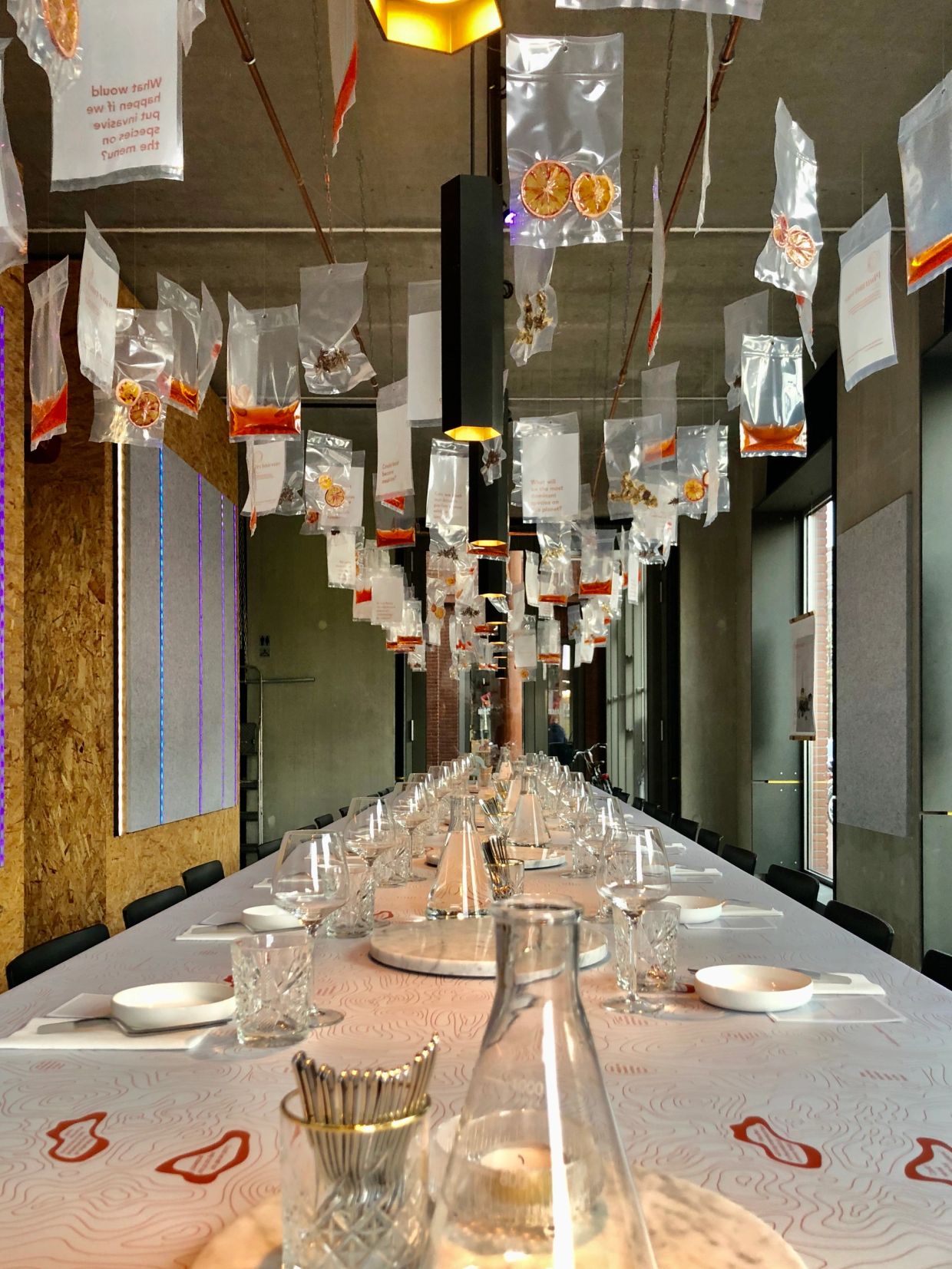 Long dining table with hanging plastic bags containing dried items and text.