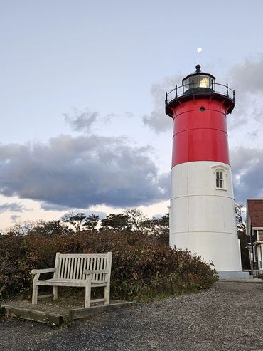 Red and white lighthouse beside a wooden bench under a cloudy sky.