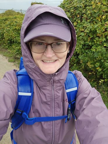 Smiling woman in purple rain jacket and cap with blue backpack outdoors.