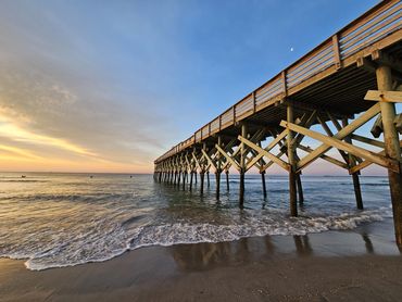 Wooden pier stretching over calm ocean waters during sunset.