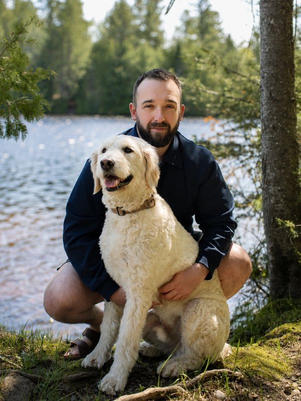 Man crouching by a lake with a happy golden retriever dog.