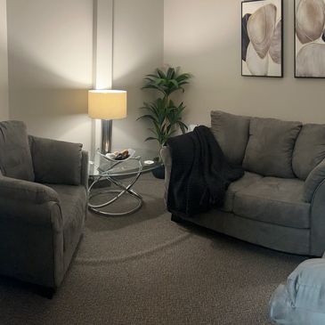 A couch, two chairs, warm lamps, and abstract art furnish the Talk Therapy Room at NCS.