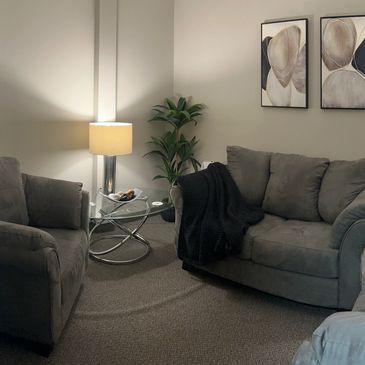A couch, two chairs, warm lamps, and abstract art furnish the Talk Therapy Room at NCS.