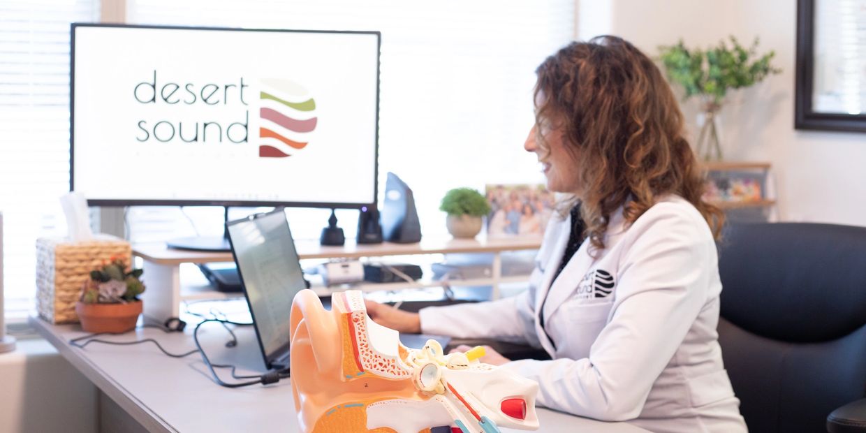 Dr Heather Smith, audiologist working at desk with logo on screen.