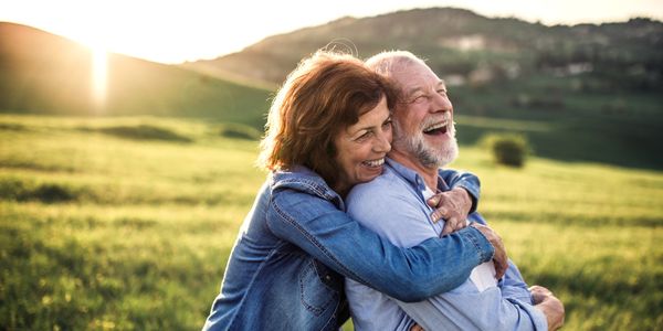 A couple is outdoors and are smiling and holding each other. They love hearing each other.