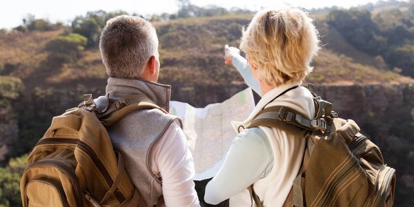 An older couple is on an outdoor hike looking at a map. They are the sound sounds of nature.