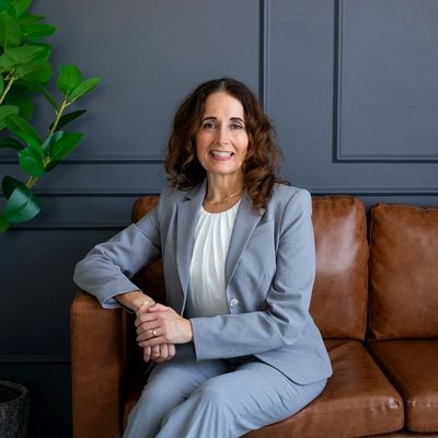 Photo of Dr. Heather Smith, Audiologist in a gray suit, sitting on a brown sofa.