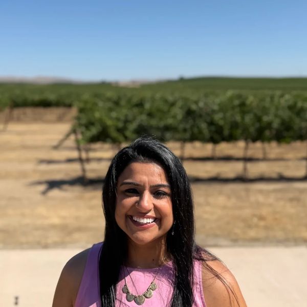 Smiling woman in pink top outdoors with vineyard background.