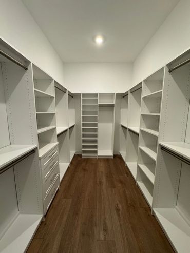Spacious walk-in closet with white shelves and wooden flooring.