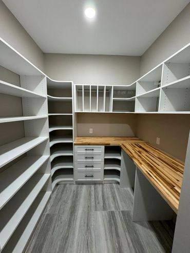 Modern walk-in closet with white shelves and wooden countertops.