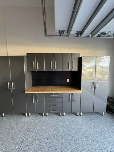 Modern gray garage cabinets with a wooden countertop and black backsplash.