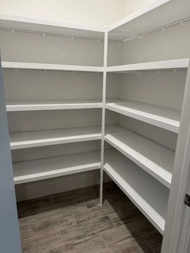 Empty white corner shelves in a small closet with wood-patterned tile floor.