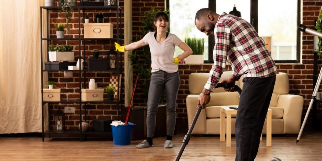 Couple cleaning their living room together, sharing a joyful moment.